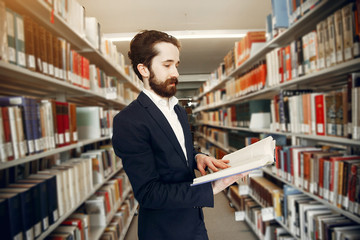 Man in a library. Guy in a black suit. Student with a books.