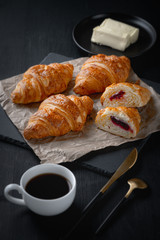  Fresh croissants with coffee and butter on a black wooden table.