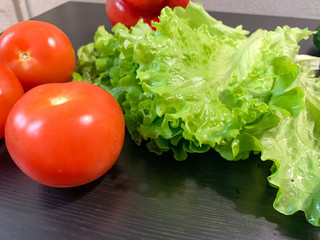 Vegetables for salad on a dark wooden table, tomatoes, peppers, cucumbers, onions and lettuce leaves. Healthy food, proper nutrition.