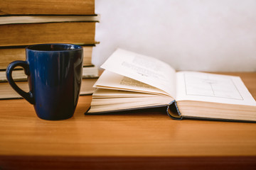 an expanded book, a blue cup and a stack of books on a table with a white background with place for text