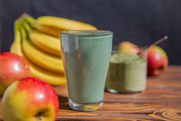 The concept of food and drink, diet and nutrition. Healthy green vegan smoothie with banana, spirulina and ripe apple for summer detoxification