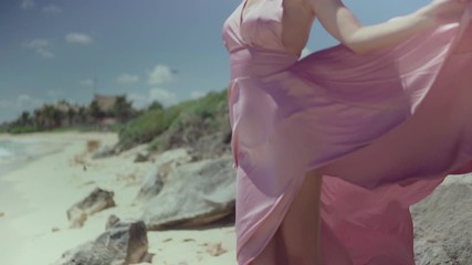 Beautiful fashionable woman in a pink dress posing in front of the camera on the seashore.