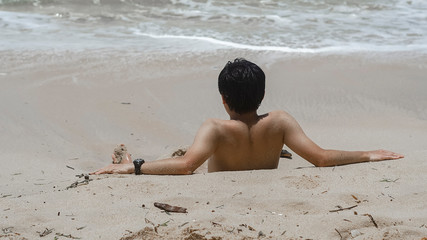 Asian man lies on the sand at the beach and enjoys a vacation