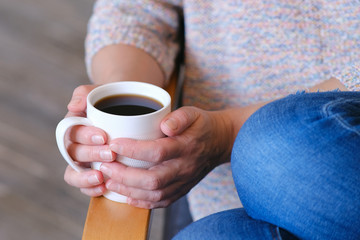 Hot coffee in a Cup. The girl holds a Cup of coffee in her hands. Warms your hands. Sitting in a chair at home in quarantine.