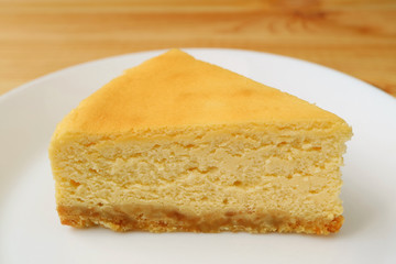 Slice of homemade creamy yellow plain baked cheesecake on a white plate