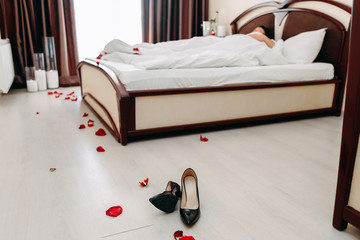 Scattered women's shoes in a hotel room on the background of the bed. Romantic atmosphere.