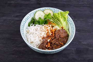 Stewed beef meat with noodles, lettuce leaves and fresh cucumbers