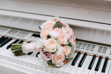 A beautiful wedding bouquet of roses and eucalyptus lies on a white piano. Details of wedding day. Attributes of the bride