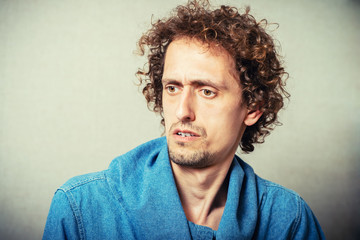 Curly young male resentment and bad mood. On a gray background