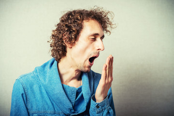 The curly-haired man yawning gesture. On a gray background.