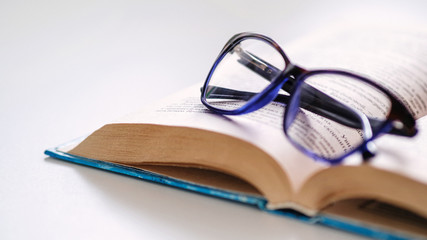 Reading glasses are located on the spread of the book lying on the sofa. The book is an excellent leisure time during the quarantine period.