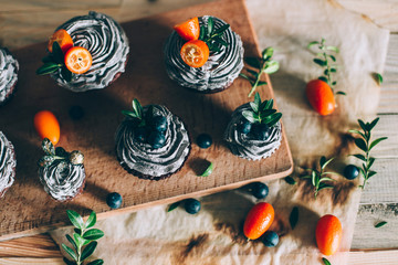 Chocolate muffins decorated with blueberry cream with berries lie on a wooden rack. Appetizing pastries for days