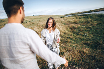 Beautiful loving couple having fun, cuddling, smiling on sky background in field. The guy and the girl hipster travel