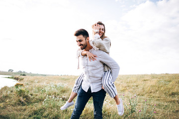 Beautiful loving couple having fun, cuddling, smiling on sky background in field. The guy and the girl hipster travel