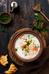 Warm Finnish creamy soup with salmon and vegetables in old ceramic bowl on old wooden background. Rustic style. Top view.