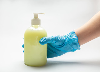 A hand in a blue medical glove holds a bottle with a dispenser with yellow liquid soap standing on a white background. Horizontal orientation.