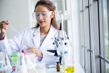 Attractive young Asian scientist woman lab technician assistant analyzing sample in test tube at laboratory. Medical, pharmaceutical and scientific research and development concept.