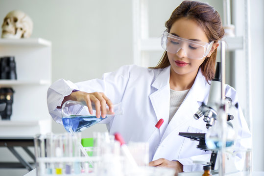 Attractive young Asian scientist woman lab technician assistant analyzing sample in test tube at laboratory. Medical, pharmaceutical and scientific research and development concept.