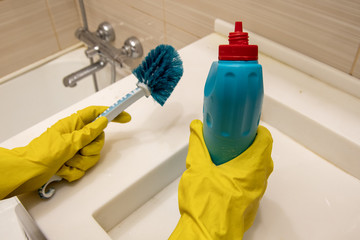Hands in yellow gloves hold cleaning agent and blue sponge on the handle for cleaning the bathroom. The concept of homework, disinfection