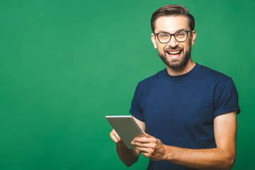 Happy young man in casual shirt and glasses standing and using tablet over green background