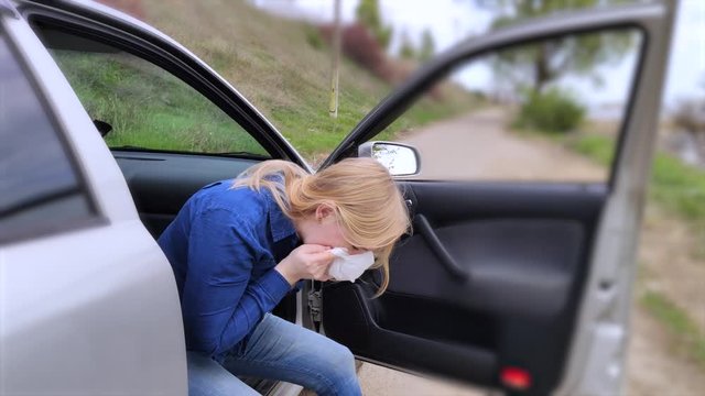 The blonde girl became ill from driving a car. Vomiting forced her to look out of the car so that the vomit would not enter the passenger compartment. The girl suffers from kinetosis, motion sickness.