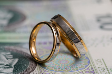 Gold wedding rings surrounded by a stack of Polish banknotes.