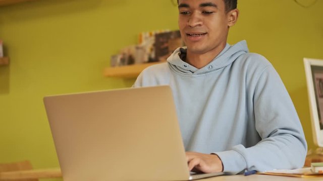 Pleased happy handsome young african boy student studying doing homework using laptop computer.