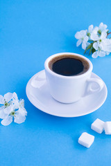 Black coffee in the white cup and  flowering tree branches on the blue background. Location vertical. Copy space.