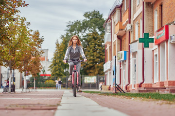 The girl rides a bicycle on the sidewalk near the pharmacy.