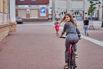 A young girl in a tracksuit rides around the city on a bicycle and turns around.