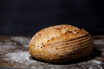 Rustic bread with seeds on a wooden table in flour, black background. Multi-grain bread with sesame, flax and sunflower seeds