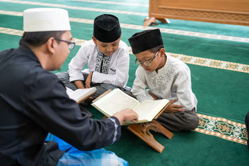 teacher is teaching muslim kid how to read holy quran in the mosque
