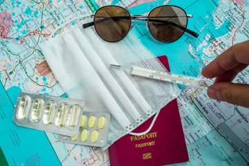Passport, surgical mask, mercury thermometer, pills and sunglasses on a map, showing travel trends during corona virus pandemic era
