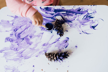 Close up top view of baby toddler hand making mess with purple paint on the table. 