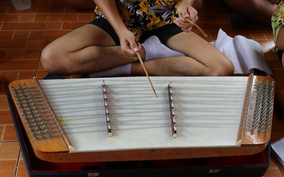 A student boy is playing Khim on dark floor, Thailand. Khim is Thai insrument made from wood broad and strings, it's shape look like chinese dulcimer.