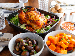 Decorated festive table with whole roasted chicken, salad, pumpkin, beans and walnut. The concept of family dinner or Thanksgiving celebrate.