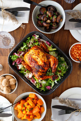 Decorated festive table with whole roasted chicken, salad, pumpkin, beans and walnut. The concept of family dinner or Thanksgiving celebrate.