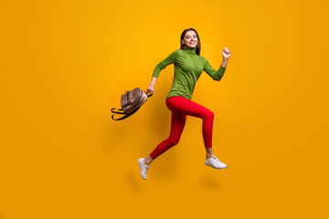 Fototapeta na wymiar Full body profile photo of funky pretty lady jumping high holding cool youngster bag rushing home after studying wear casual green jumper red pants isolated yellow color background