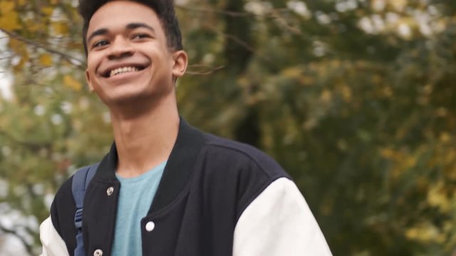 Handsome cheery happy young african guy student walking outdoors waving to friends.