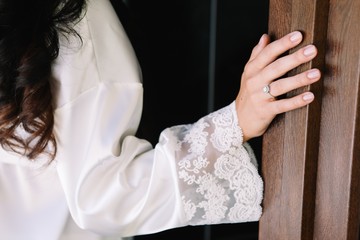 Bride in wedding robe is standing near door. Wedding ring on the hand.