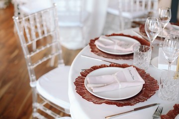 Wedding. Banquet. Glass table with pink and white flowers and red and white plates on it, served with cutlery, flowers and crockery.