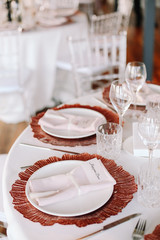 Wedding. Banquet. Glass table with pink and white flowers and red and white plates on it, served with cutlery, flowers and crockery.