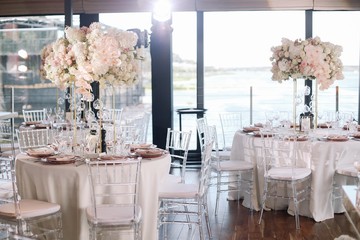 Wedding. Banquet. The chairs and round table for guests, served with cutlery, flowers and crockery and covered with a tablecloth with pink and white flowers and red plates