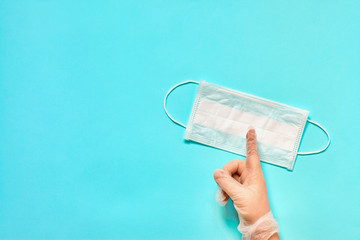 A hand in glove showing Attention sign and medical face mask on blue background. Virus or flu prevention concept. Top view, copy space