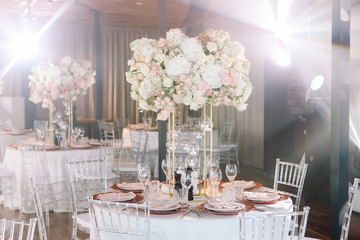 Wedding. Banquet. The chairs and round table for guests, served with cutlery, flowers and crockery and covered with a tablecloth with pink and white flowers and red plates