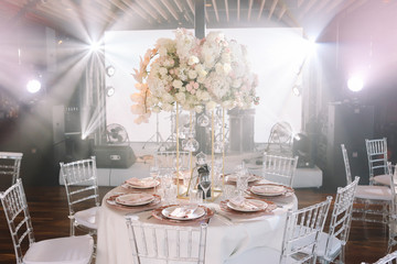 Wedding. Banquet. The chairs and round table for guests, served with cutlery, flowers and crockery and covered with a tablecloth with pink and white flowers and red plates