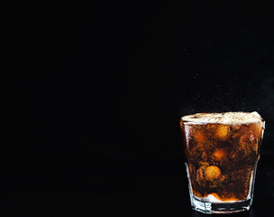 Cool, non-alcoholic, carbonated cola drink. Refreshing drink with sparkling water, a full glass with cola bubbles above the glass, the drink overflows. Dark background, close-up with copy space