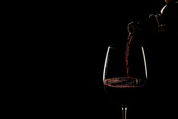 Mano con una botella de vino sirviendo una copa de vino tinto sobre fondo negro aislado. Vista de frente y vista de cerca. Copy space
