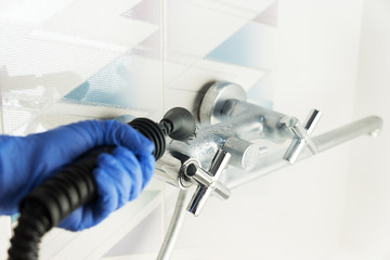 cleaning  chrome tap in bathroom with steam generator, hand in blue glove holds steam genetator and hose with brush, which produces steam, home cleaning concept, mold and calcium control