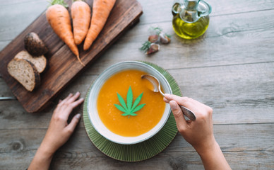 Top view of young woman eating carrot soup with marijuana oil and leaf inside - Food and healthy...
